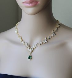 a woman wearing a necklace with green and white stones on the bottom, along with an emerald pendant