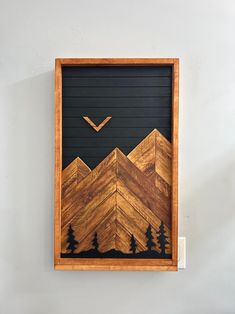 a wooden frame hanging on the wall with mountains and pine trees painted on it's side