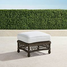 a white ottoman sitting on top of a cement floor next to a green hedge covered wall