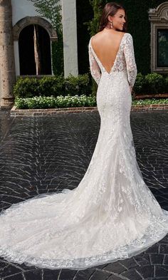 a woman in a white wedding dress standing on a cobblestone road with her back to the camera