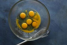 four eggs are in a glass bowl on a blue surface with a whisk