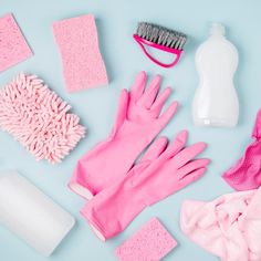 pink cleaning supplies laid out on a light blue surface, including gloves and sponges