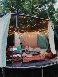 an outdoor tent is set up with clothes and lights on the trees in the background