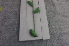 two green plastic flowers are on a piece of wood that is laying on the ground