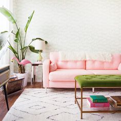 a living room with a pink couch and green ottoman in the corner, next to a large potted plant