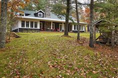 a house in the woods with lots of leaves on the ground and trees around it