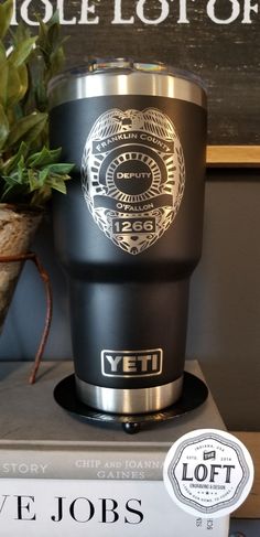 a black and silver coffee cup sitting on top of a stack of books next to a potted plant