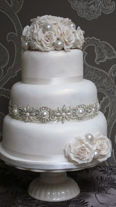 a three tiered wedding cake with white flowers and pearls