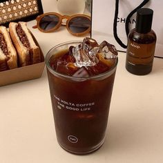 an iced drink with ice sits on a table next to sunglasses and a box of bread