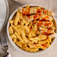 a white bowl filled with pasta and chicken on top of a table next to a fork