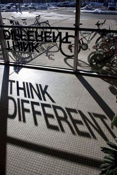 the shadows of bicycles are cast on the floor in front of a glass window that reads think different