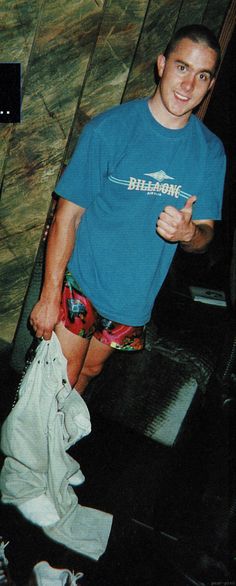 a man in blue shirt and shorts standing next to a skateboard on the ground