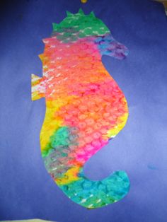 a seahorse made out of plastic beads on a blue paper sheet with yellow and green dots