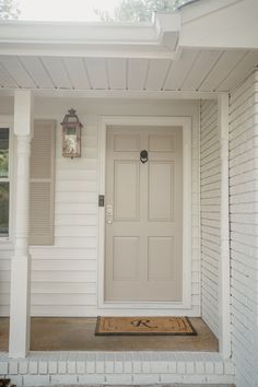 the front door of a white house with shutters and a light fixture on it