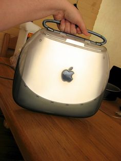 an apple toaster sitting on top of a wooden table next to a person's hand