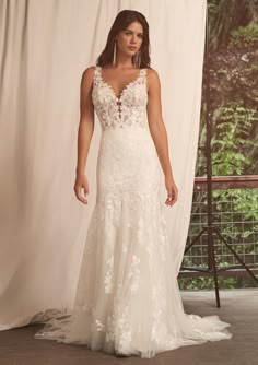 a woman standing in front of a white backdrop wearing a dress with flowers on it