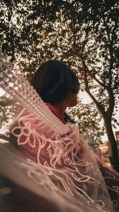 a woman standing under a tree wearing a shawl and looking off into the distance