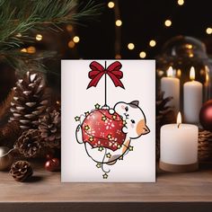 a christmas card with a sheep hanging from it's side next to candles and pine cones