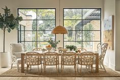 a dining room table and chairs in front of large windows with potted plants on them