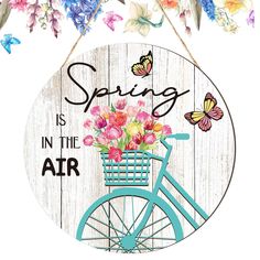 a sign that says spring is in the air on a bicycle with flowers and butterflies