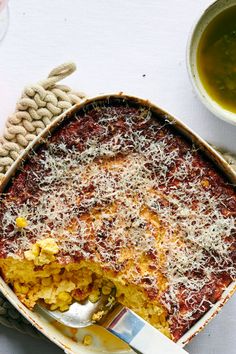 a casserole dish with cheese on top and a spoon in the bowl next to it