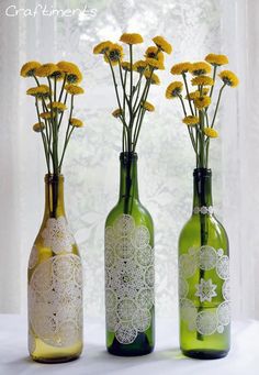 three green bottles with yellow flowers in them