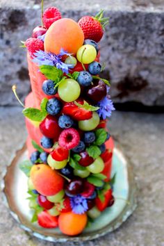 a cake with fruit on it sitting on top of a glass plate next to a stone wall