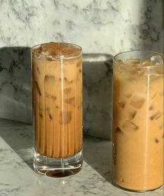 two glasses filled with liquid sitting next to each other on a marble counter top in front of a marble wall