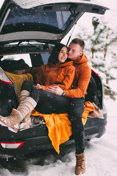 a man and woman sitting on the back of a car in the snow with their trunk open