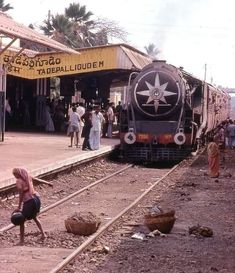 people are standing on the side of a train track as it pulls into a station