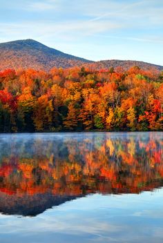 the mountains and trees are reflected in the still waters of a lake surrounded by autumn foliage