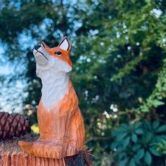 a statue of a fox sitting on top of a tree stump next to a pine cone