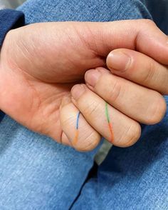 a person's hand with two colored crayons on their thumb and fingers