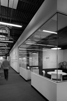 an office with glass walls and white desks in the foreground is a man walking by