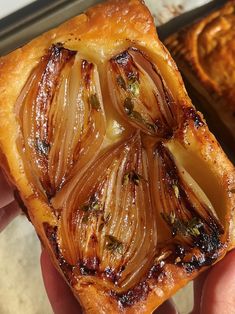 a hand holding a pastry with onions on it