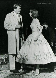 an old black and white photo of a man standing next to a woman in a dress