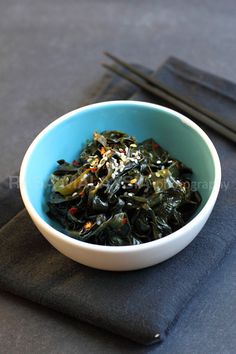 a blue bowl filled with green vegetables on top of a table next to chopsticks