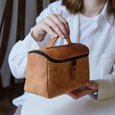 a woman is holding a brown leather bag