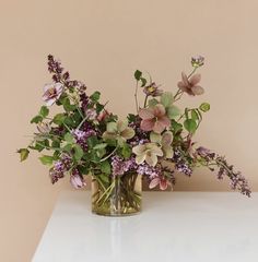 a vase filled with lots of flowers on top of a white table next to a wall