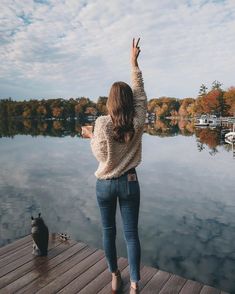 a woman standing on a dock with her arms in the air and looking out at water