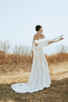 a woman in a white wedding dress holding a scarf over her shoulder and looking off into the distance