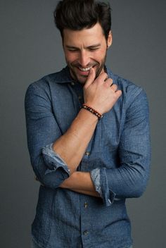 a man is smiling and posing with his hands on his chin while wearing a blue shirt