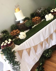 a table topped with cakes and cupcakes covered in greenery