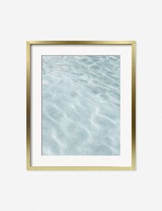 a gold framed photo hanging on a wall above the ocean water in front of a white background