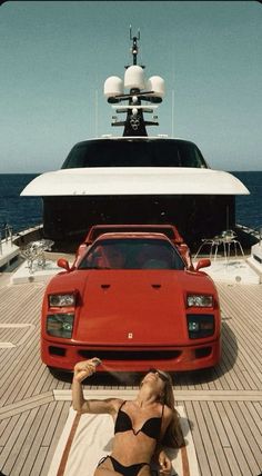 a woman laying on top of a towel next to a red car in front of a boat