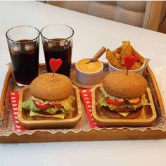 two hamburgers and fries on a tray with cups of soda, potato chips and ketchup