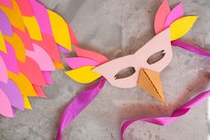 a paper mask with pink and yellow feathers