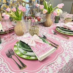 the table is set with pink and green plates, silverware, napkins, and flowers