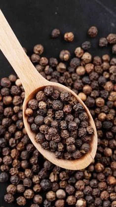 a wooden spoon filled with black pepper on top of a pile of other small spices