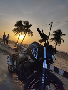 the motorcycle is parked on the side of the road near the beach as the sun sets